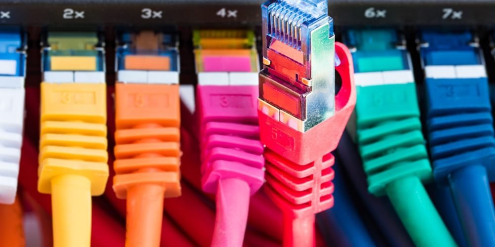 Foto de uma sequência de cabos de fibra óptica coloridos conectados em uma rede com gerenciamento OLT